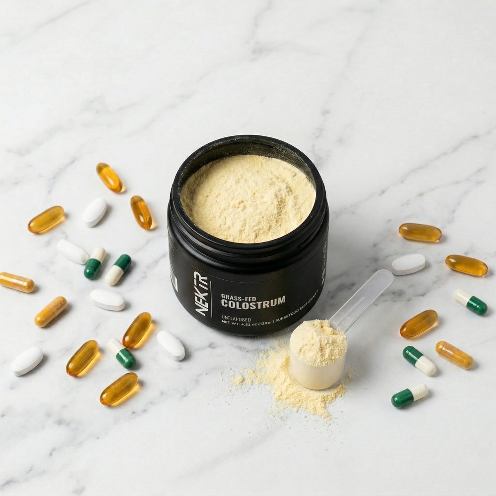 NEKTR colostrum jar open with powder and supplement capsules on marble